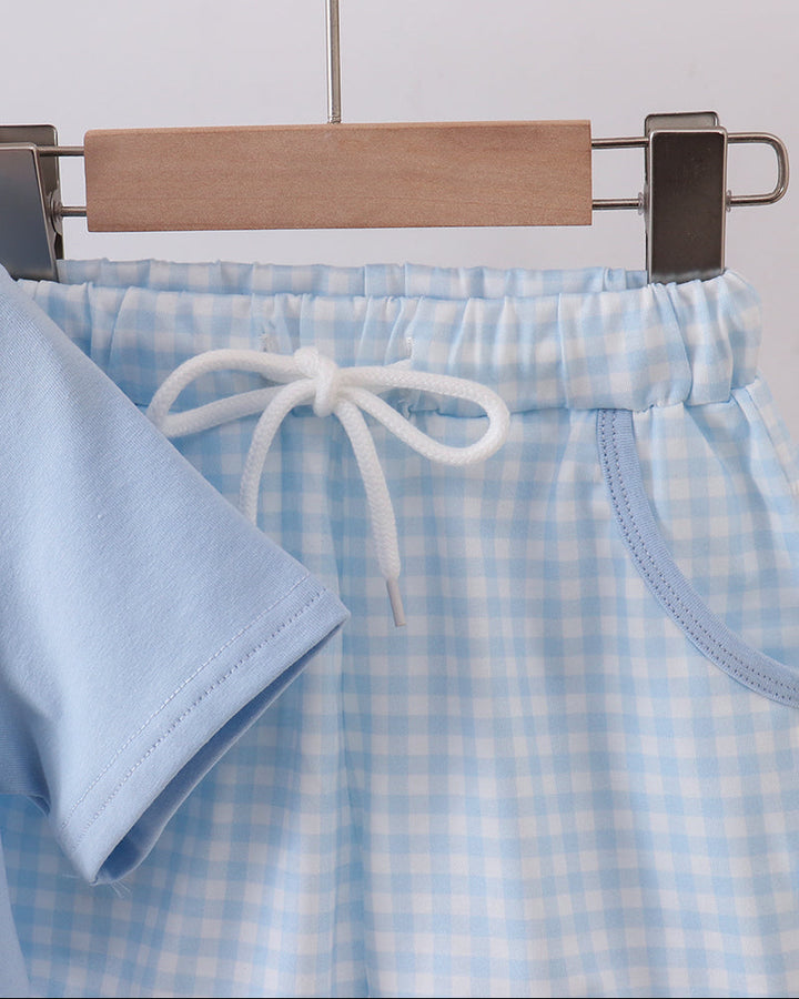 Light blue checkered shorts with a drawstring on a wooden hanger against a light gray background