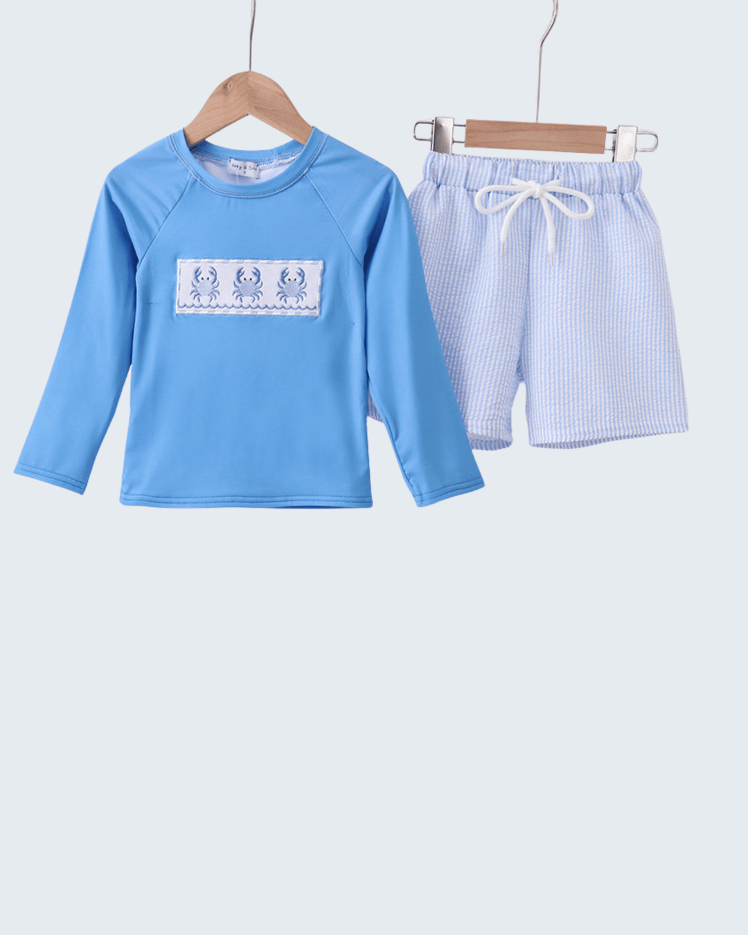 Children's blue long-sleeve shirt and shorts set on hangers against a white background