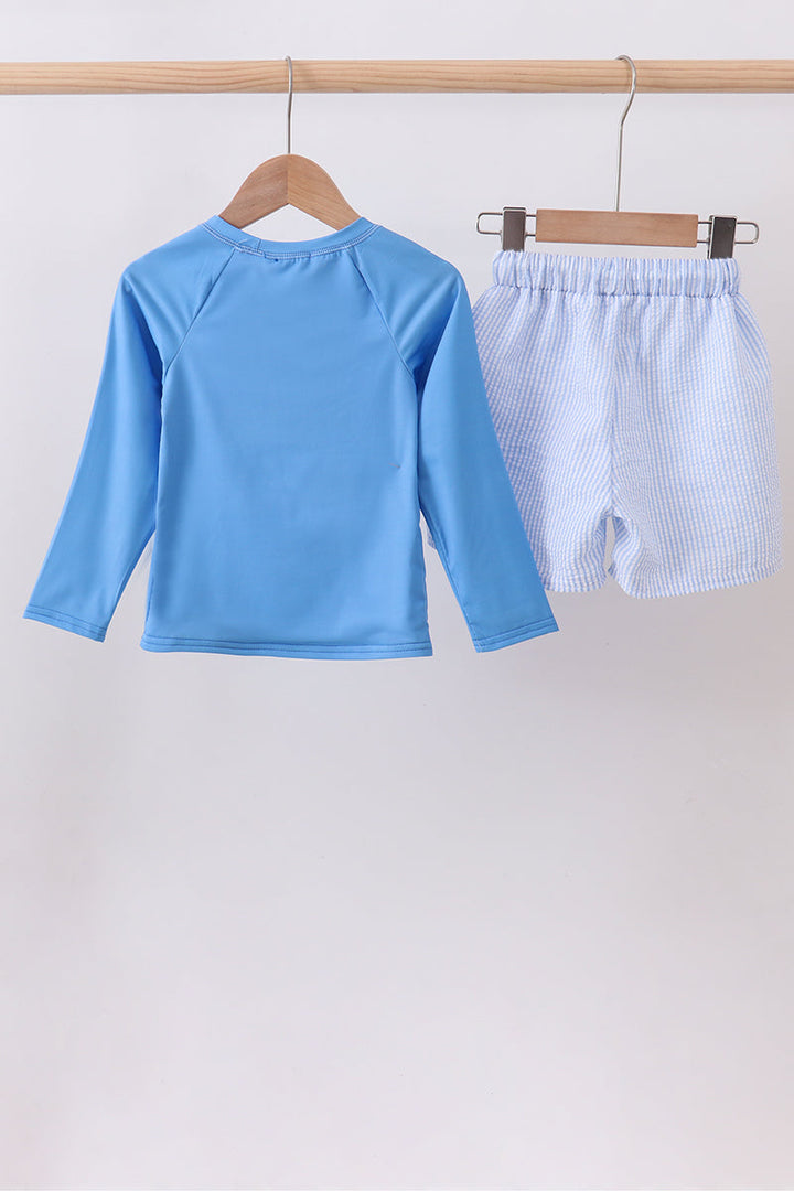 Blue long-sleeve shirt and checkered shorts on hangers against a white background