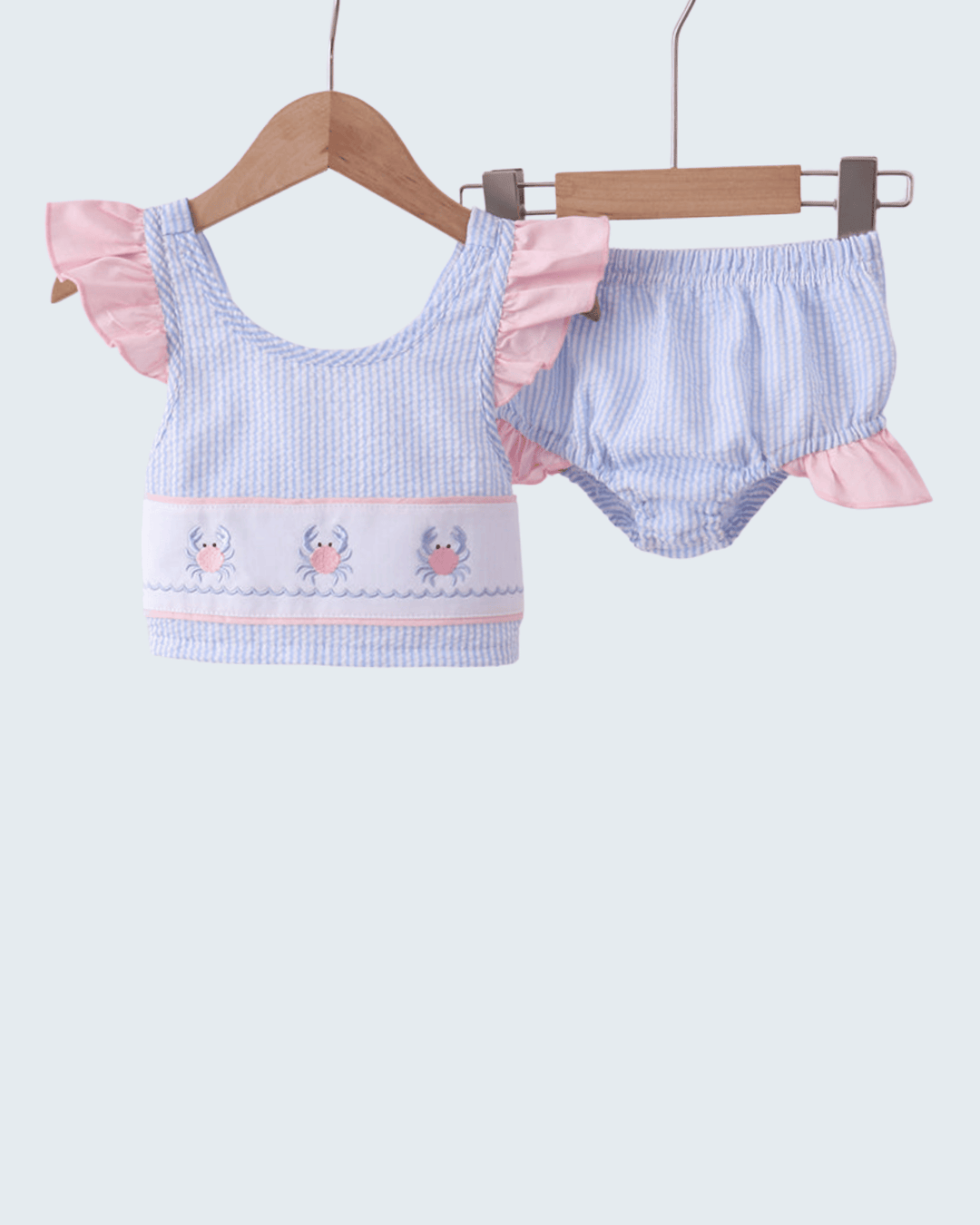 Baby girl's swimsuit with ruffled top and bloomers on a hanger against a white background