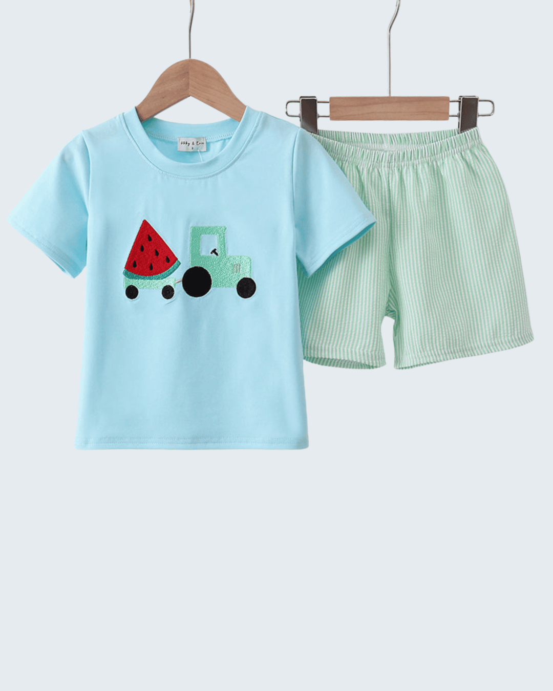 Children's light blue t-shirt with watermelon and tractor design and green shorts on a white background