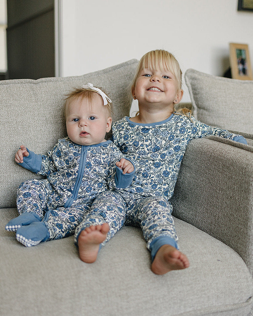 Two children in matching blue and white pajamas sitting on a couch.