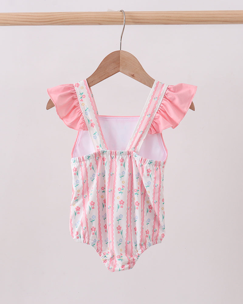Baby swimsuit with floral pattern and ruffled sleeves on a wooden hanger against a light background