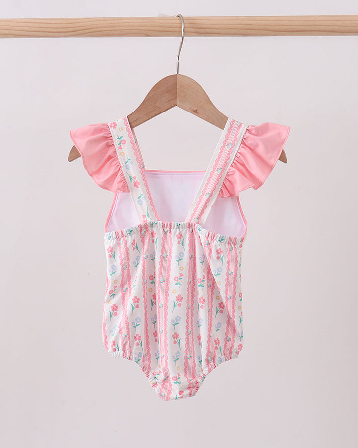 Baby swimsuit with floral pattern and ruffled sleeves on a wooden hanger against a light background