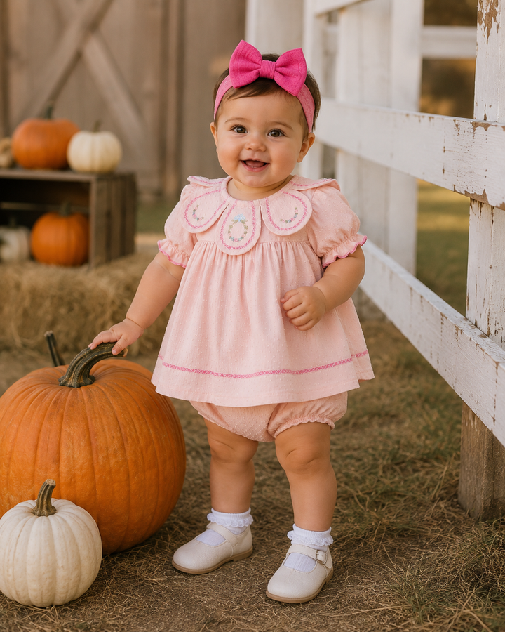 Baby wearing blush pink embroidered petal-collar dress with matching bloomers, bow headband