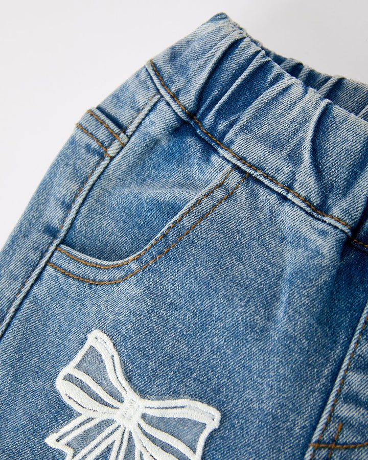 Close-up: girls denim flare jeans with white bow lace patch and stitched seams