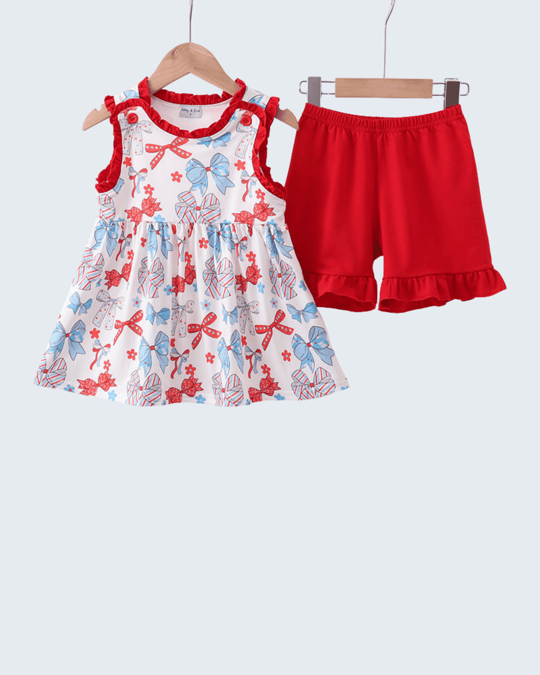 Children's dress with bow pattern and red shorts on hangers against a white background