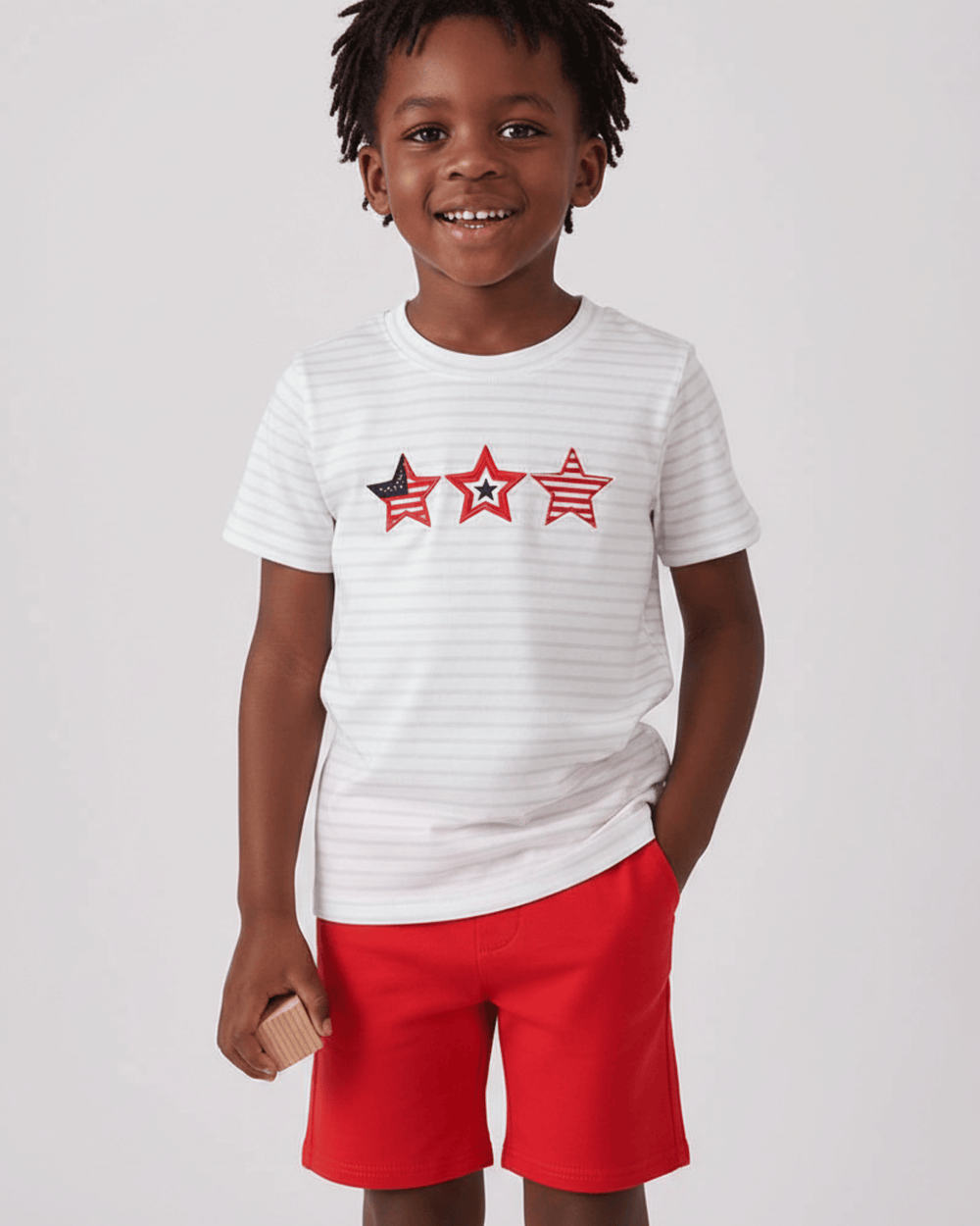 Child wearing a white t-shirt with star designs and red shorts on a light gray background