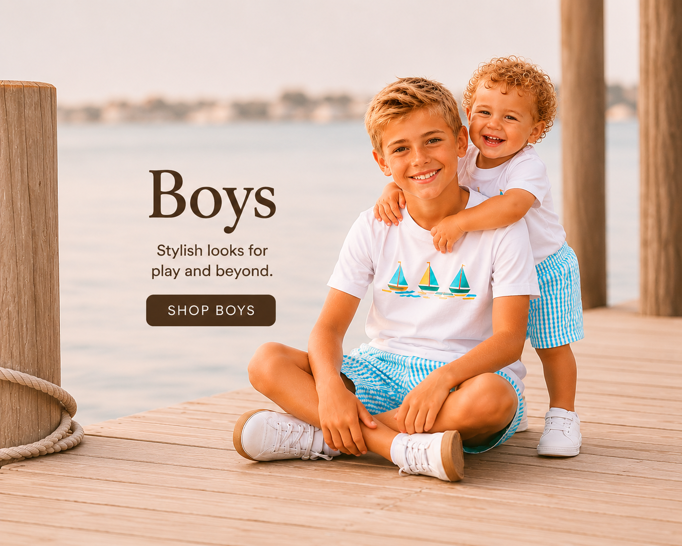 Two boys sitting on a wooden dock by the water, with text promoting boys' clothing.