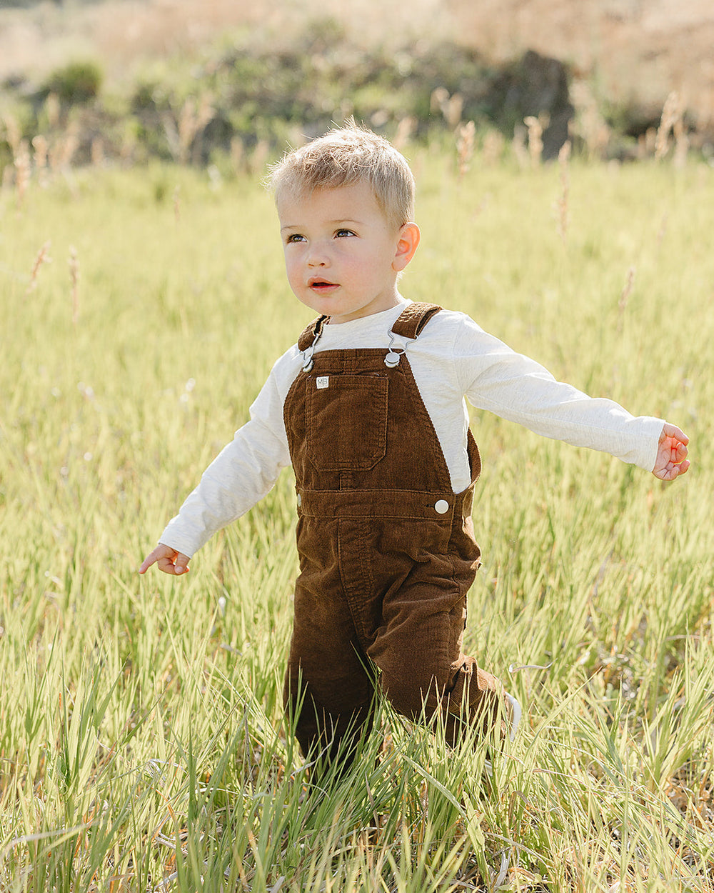 Brown corduroy overalls with suspenders, two buttons, and front patch pocket on toddler.