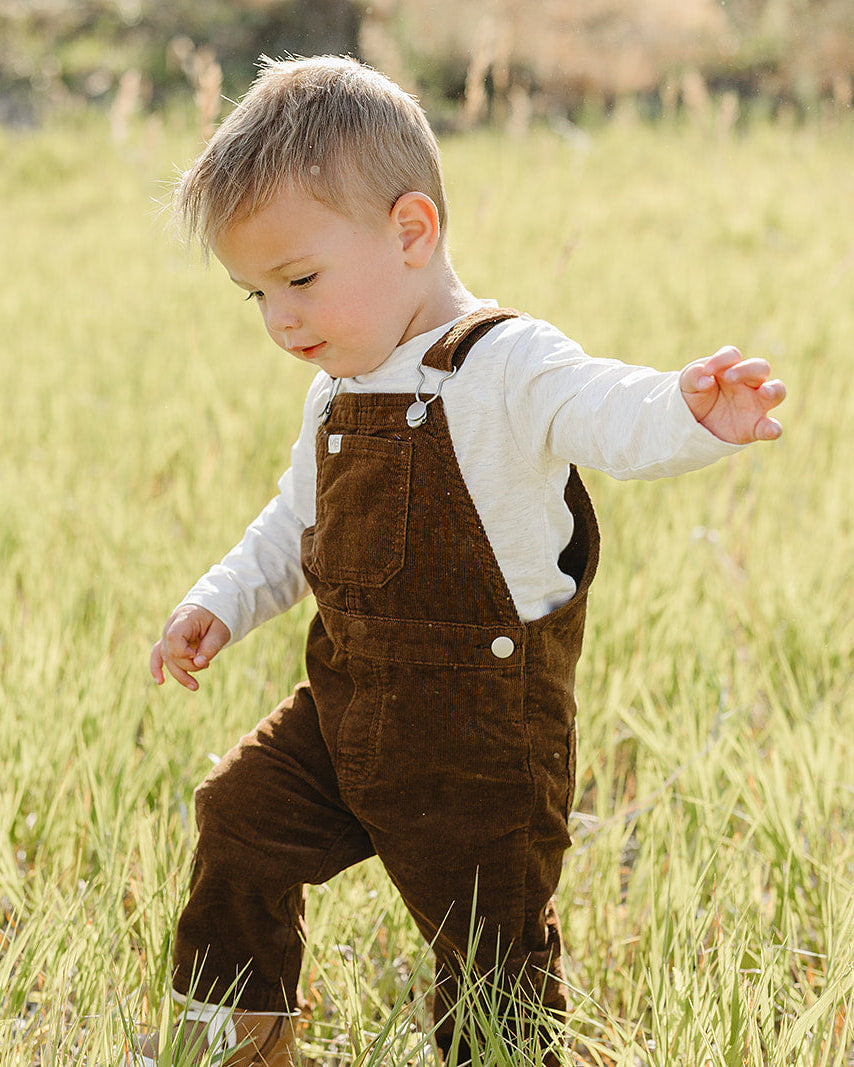 Brown corduroy overalls with adjustable straps and front pocket worn by a toddler.