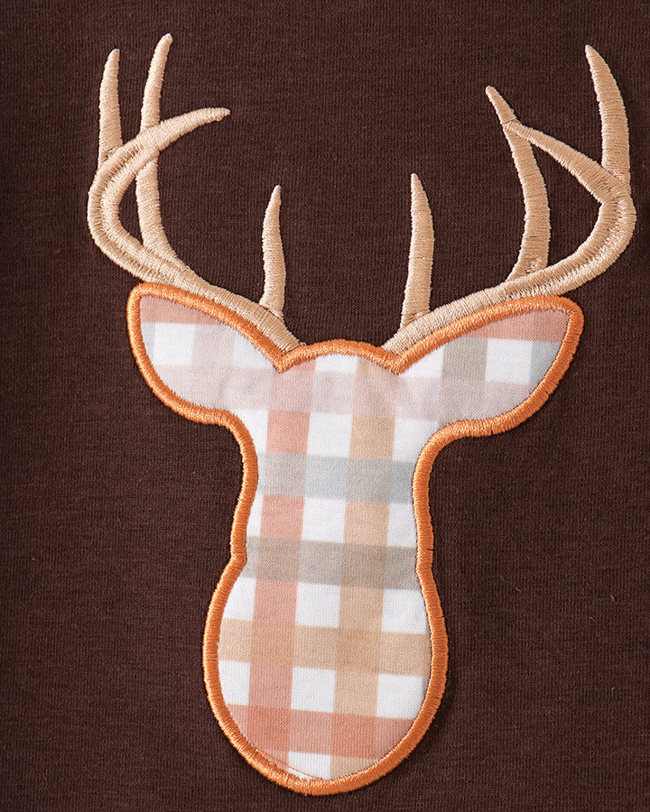 A deer head applique patch with tan antlers and a peach, white, and gray gingham patterned face, outlined in orange-brown, shown on a dark brown fabric background.