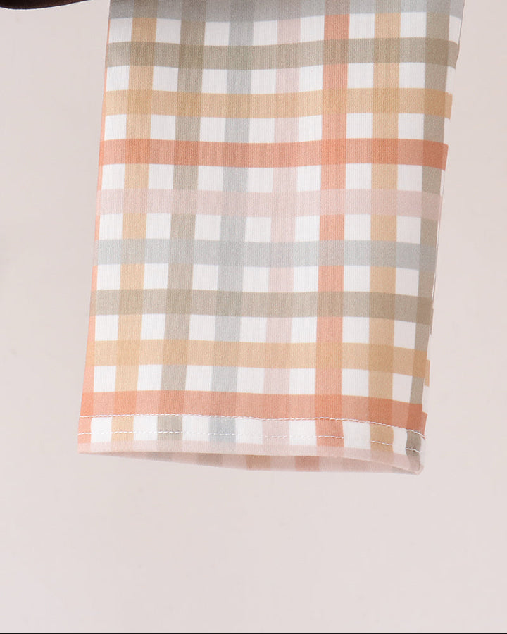 A close-up of pant leg, featuring a multi-colored gingham plaid pattern in white, peach, beige, and light gray, with a dark brown leather strap visible at the top edge.