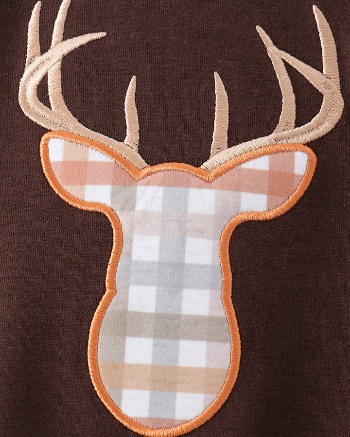 A close-up of a brown knit garment featuring an applique deer head patch with beige antlers and a beige, white, and light brown gingham patterned face outlined in orange-brown.
