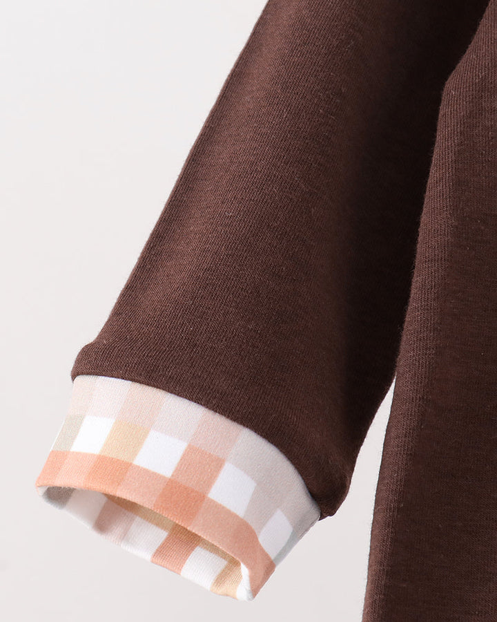 Close-up of a brown knit garment sleeve with a folded cuff showing a white, peach, and beige gingham lining, set against a plain light gray background.