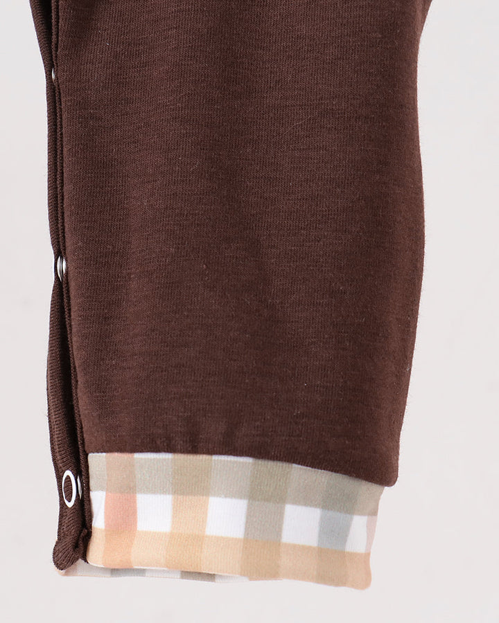 Close-up of a brown knit garment, likely a sweater or cardigan, showing the cuff with a beige, white, and light pink plaid lining.