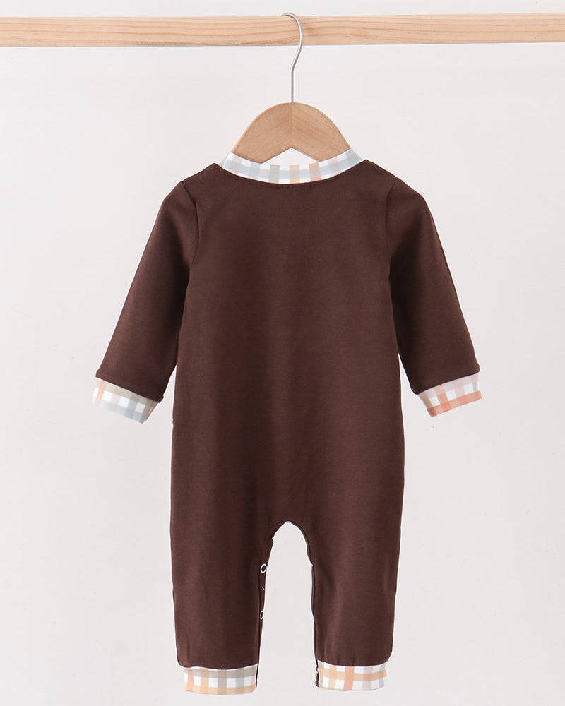 A baby long-sleeve footless romper in dark brown, hanging on a wooden hanger. The romper features contrasting light beige and white gingham trim at the collar, cuffs, and hems.