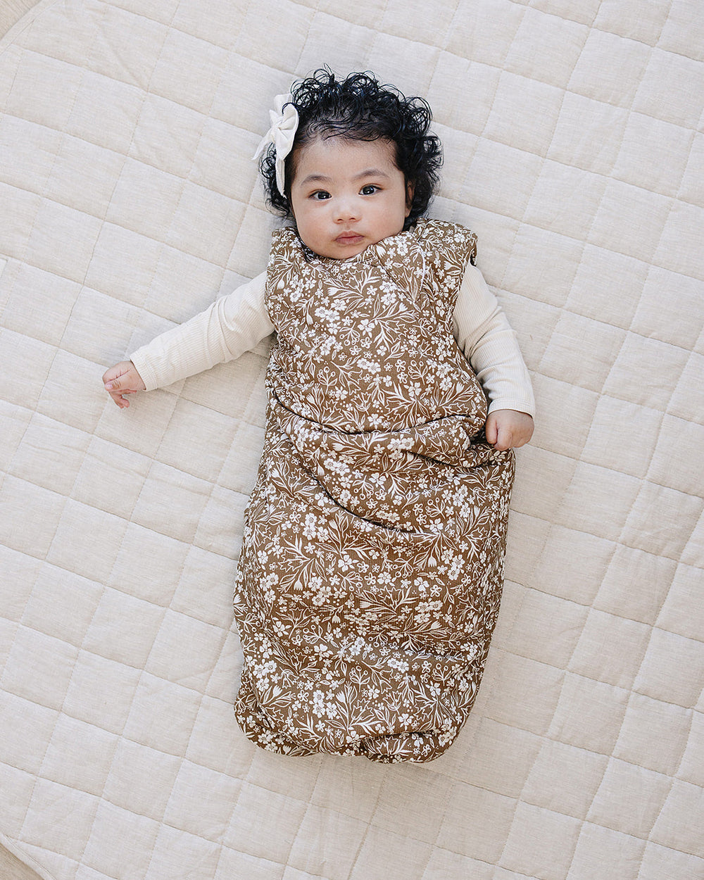 Baby lying on a quilted surface wearing a floral sleep sack