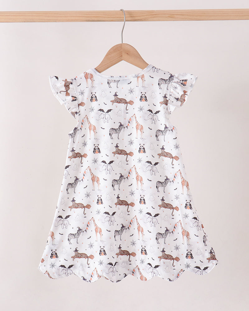 A white baby dress with a print of foxes, rabbits, and deer, hanging on a wooden hanger against a light beige background.
