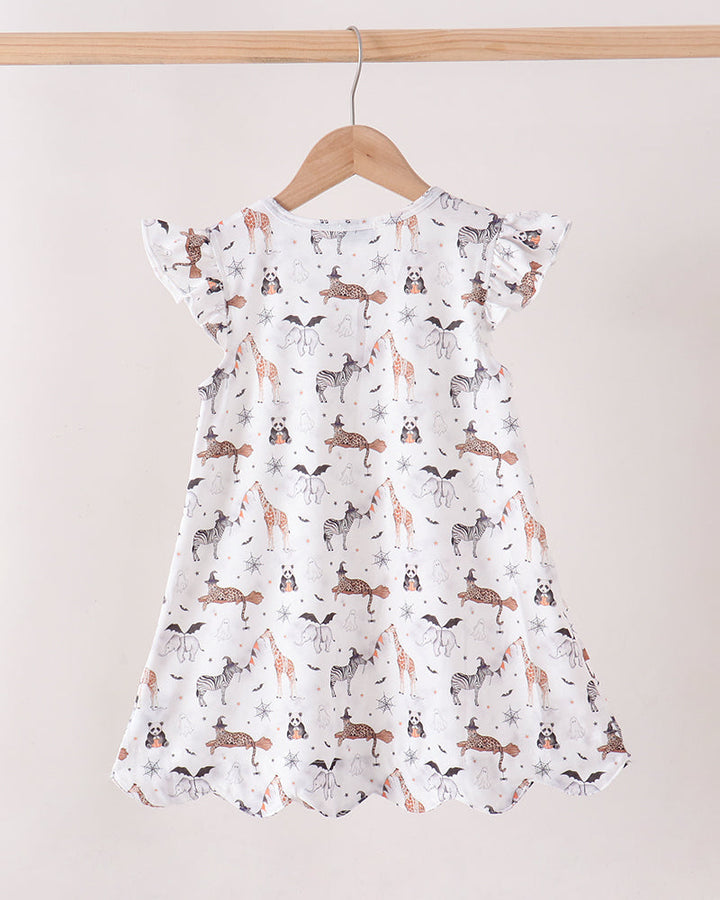 A white baby dress with a print of foxes, rabbits, and deer, hanging on a wooden hanger against a light beige background.