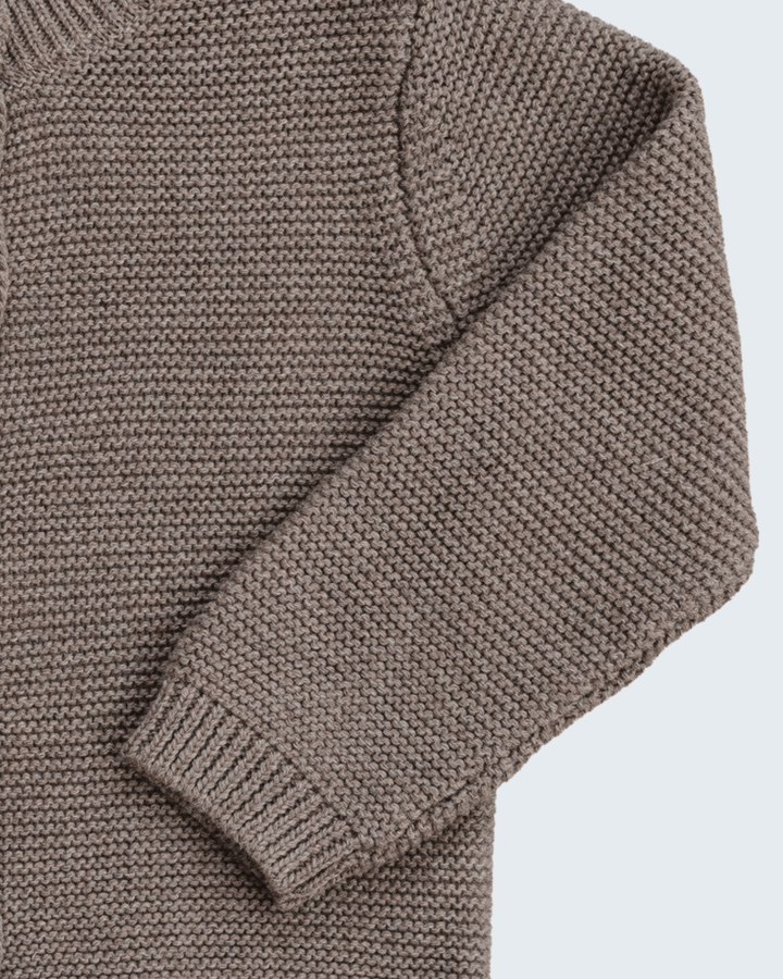 Close-up of a ribbed knit sweater in a taupe brown color, showing the texture and sleeve detail against a light gray background.