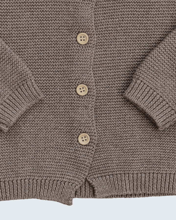 Close-up of a brown ribbed knit cardigan with four light beige buttons, showing the texture and sleeve cuffs.