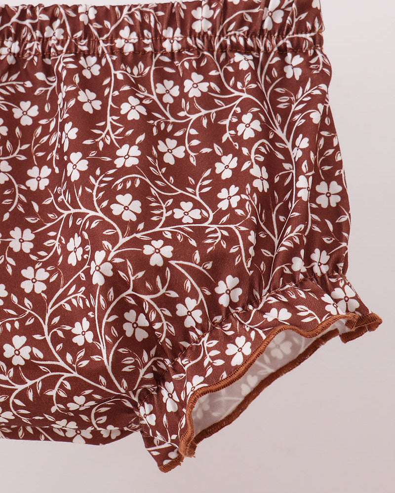 Brown and white floral print ruffled shorts with an elastic waistband, shown against a light pink background.