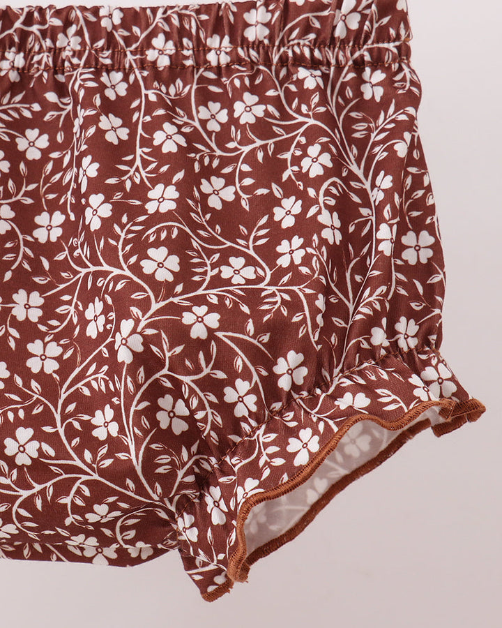 Brown and white floral print ruffled shorts with an elastic waistband, shown against a light pink background.