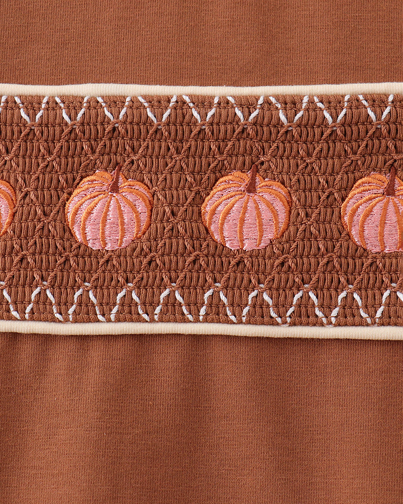 Smocked pumpkin panel on brown top with white eyelet-style trim