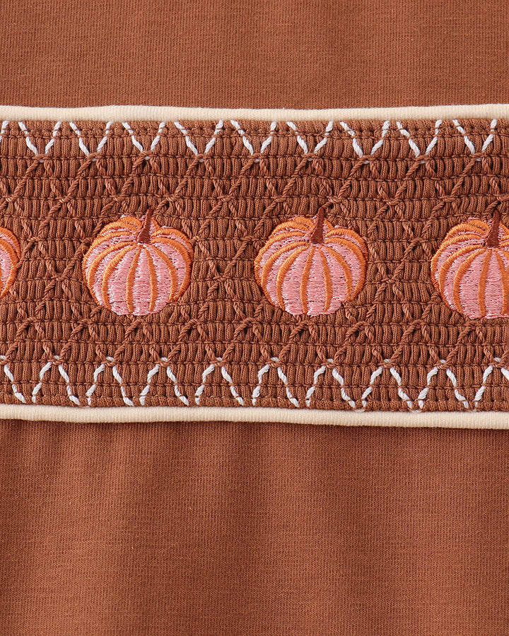 Smocked pumpkin panel on brown top with white eyelet-style trim