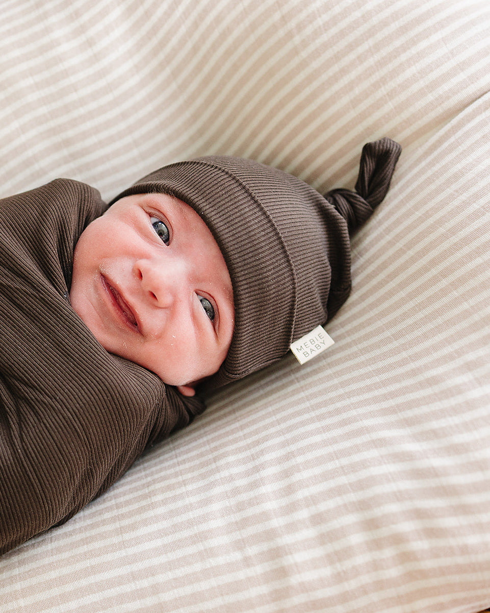Newborn knot hat in dark brown ribbed knit, worn with soft fold brim.