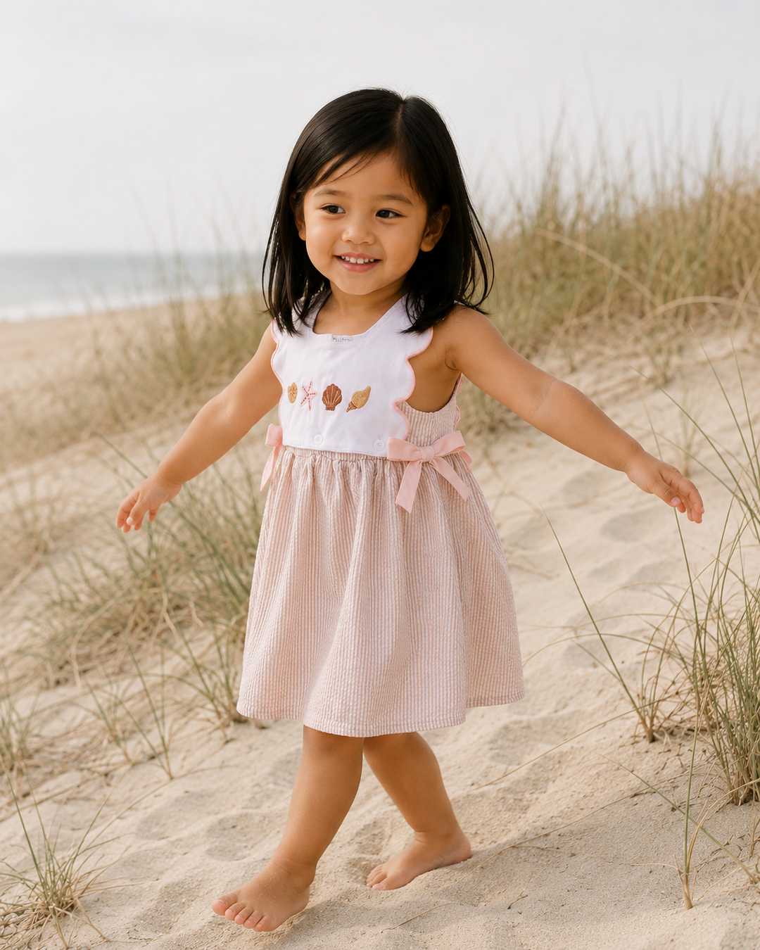 Young girl in a dress standing on a sandy beach with grasses.