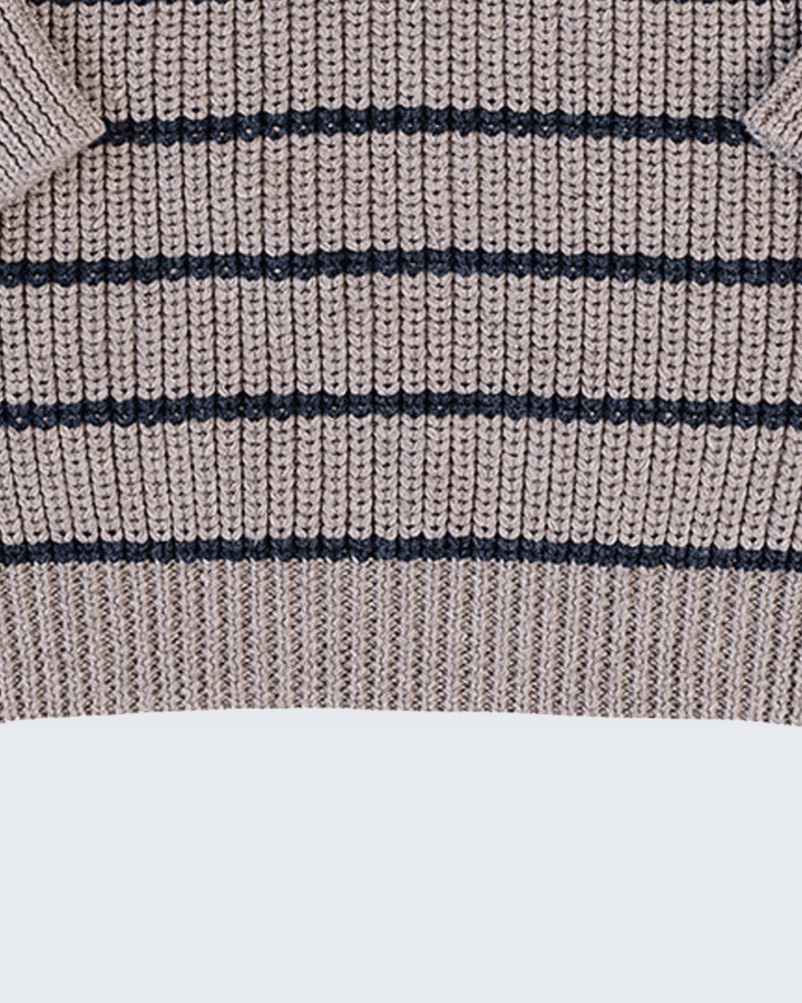 Close-up of a ribbed knit sweater showing horizontal navy stripes on a warm beige background.