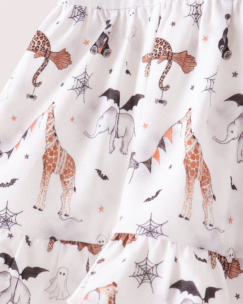 White ruffled baby skirt with a Halloween print featuring orange-brown giraffes, gray elephants, black bats, ghosts, spiderwebs, and orange stars.
