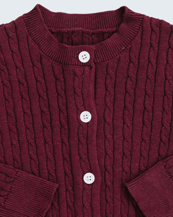 A close-up of a burgundy cable-knit cardigan sweater featuring a crew neck, three white buttons, and ribbed cuffs.