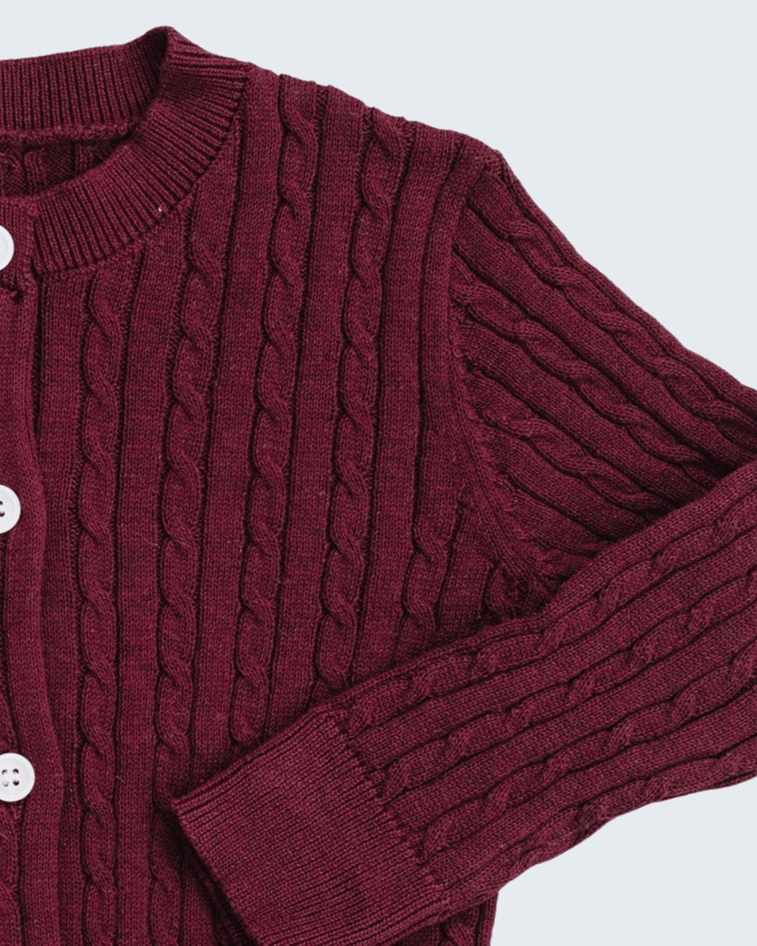 Close-up of a burgundy cable-knit cardigan sweater with white buttons, showing the detailed knit texture and ribbed collar, cuffs, and hem.