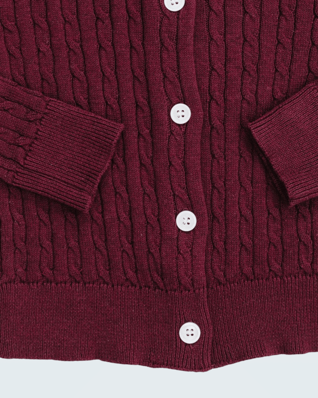 Close-up of a burgundy cable-knit cardigan sweater showing the button closure with white buttons and ribbed cuffs.