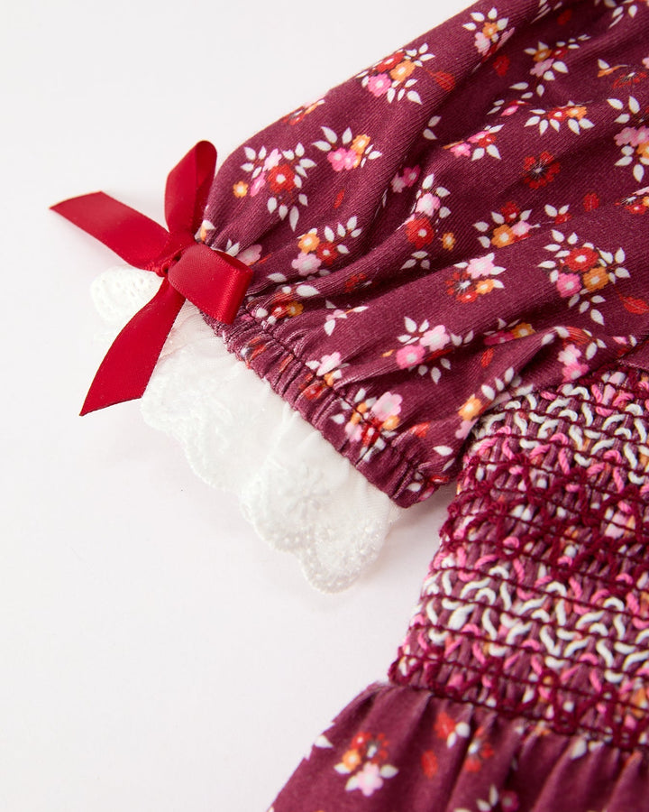 Side view of burgundy floral romper with white lace leg ruffles and red bow detail