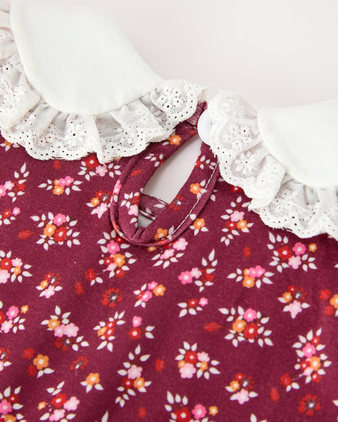 Close-up of burgundy floral bubble romper neckline with white Peter Pan collar and button placket