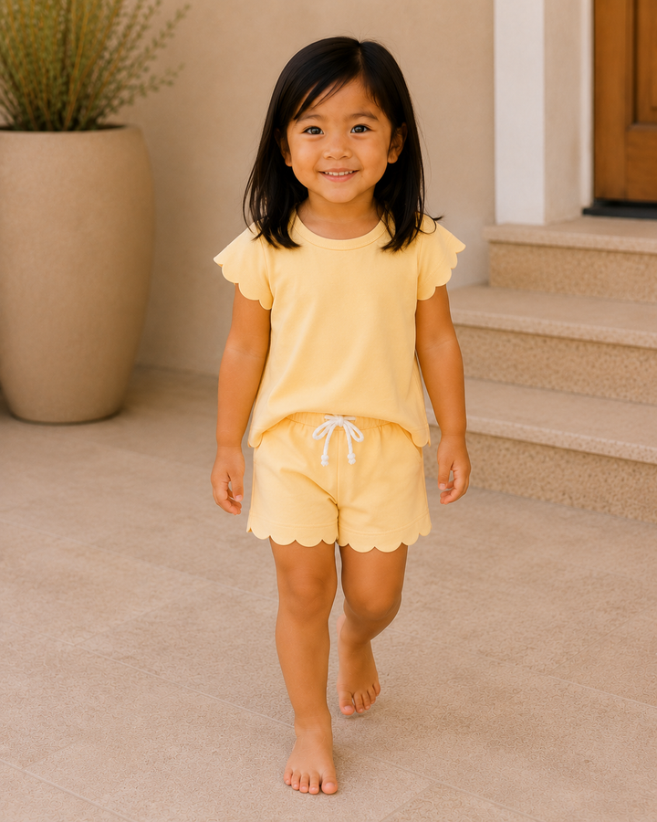 Young girl in a yellow outfit standing on a beige carpeted floor.