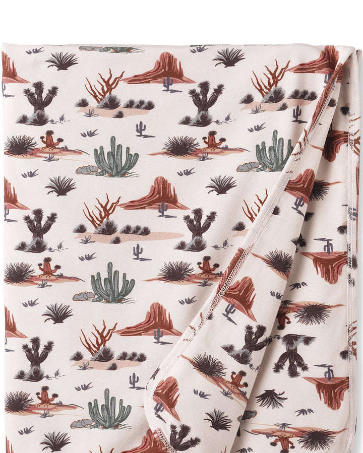 Folded baby blanket with desert landscape pattern on a white background