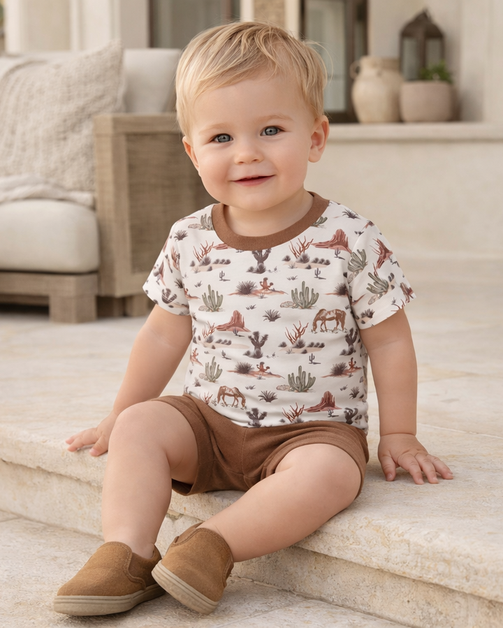 Child wearing a patterned shirt and brown shorts sitting on a staircase.