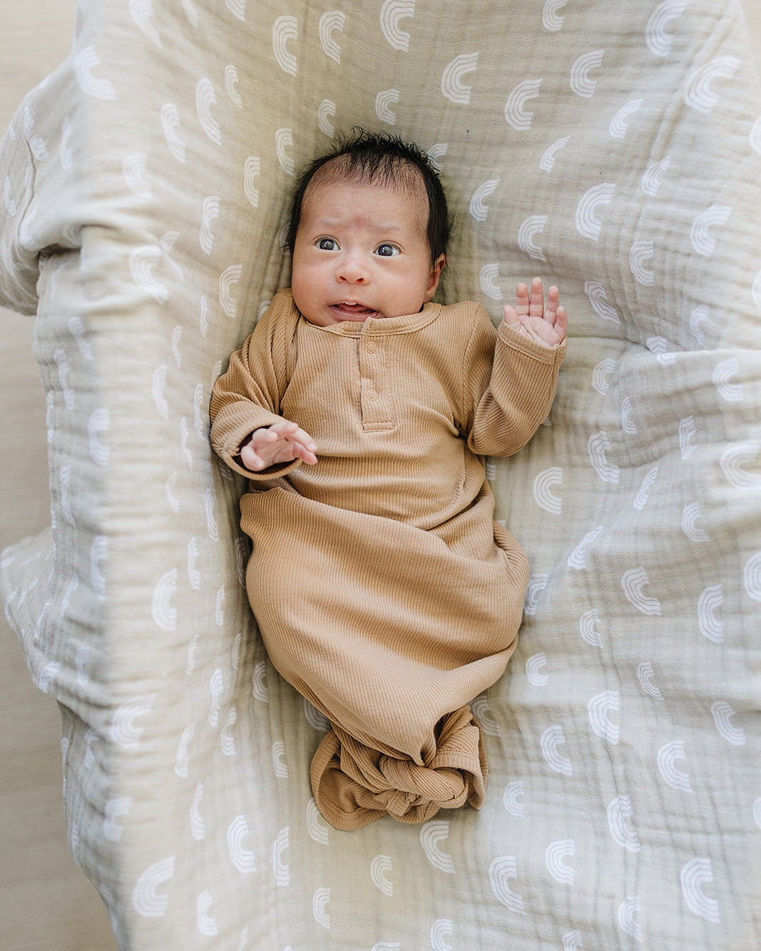 Baby in a brown knot gown lying on a textured blanket