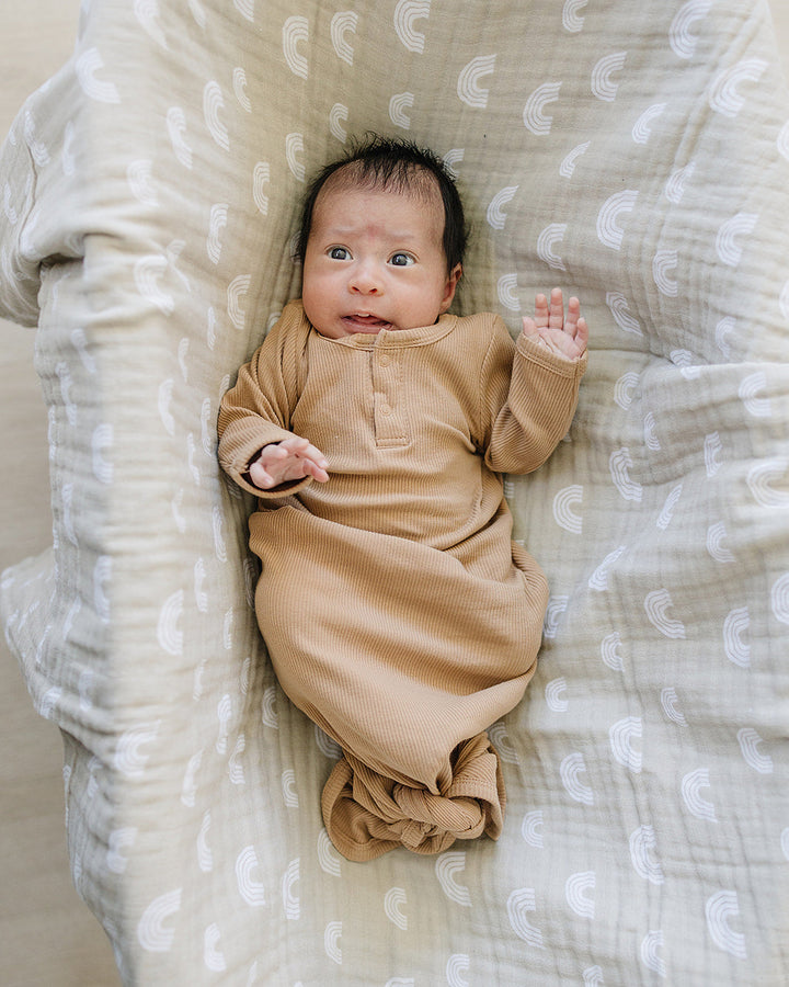 Baby in a brown knot gown lying on a textured blanket