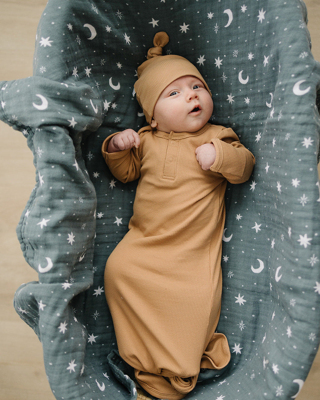 Baby in a brown knot gown lying in a green crib with star and moon pattern