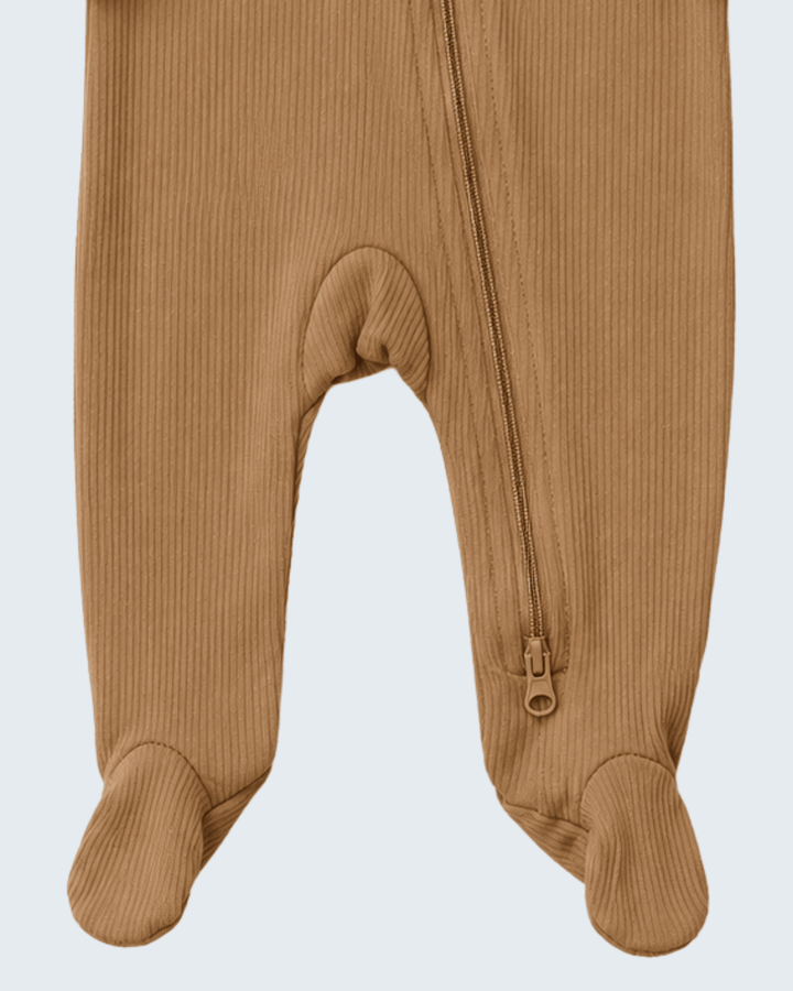 Close-up of a baby footed one-piece pajama in a warm camel brown ribbed fabric, showing the front zipper and foot cuffs against a light gray background.