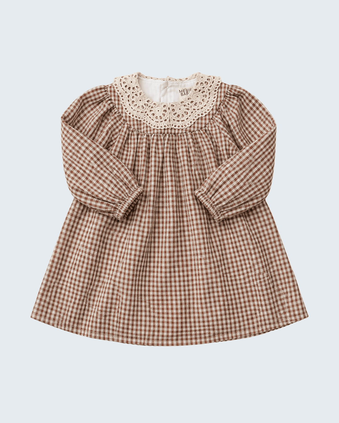 A long-sleeve baby dress with a brown and beige gingham pattern, featuring a smocked bodice and a cream-colored crochet lace collar, shown against a light gray background.