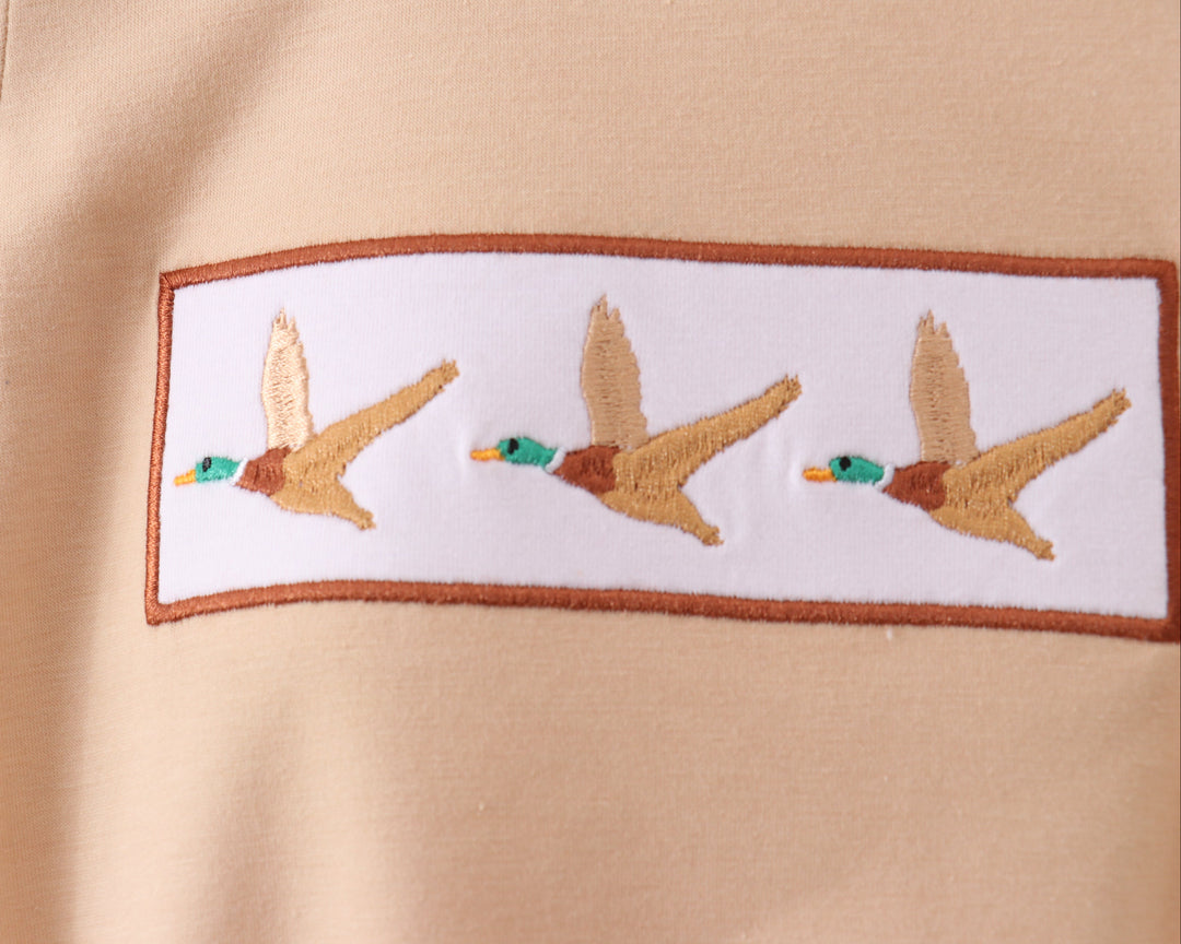 Embroidered design of three ducks on a beige fabric background