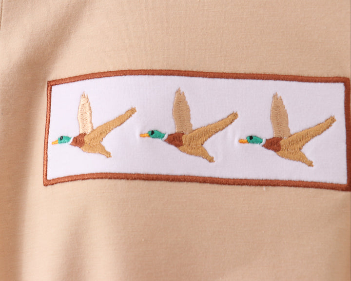 Embroidered design of three ducks on a beige fabric background