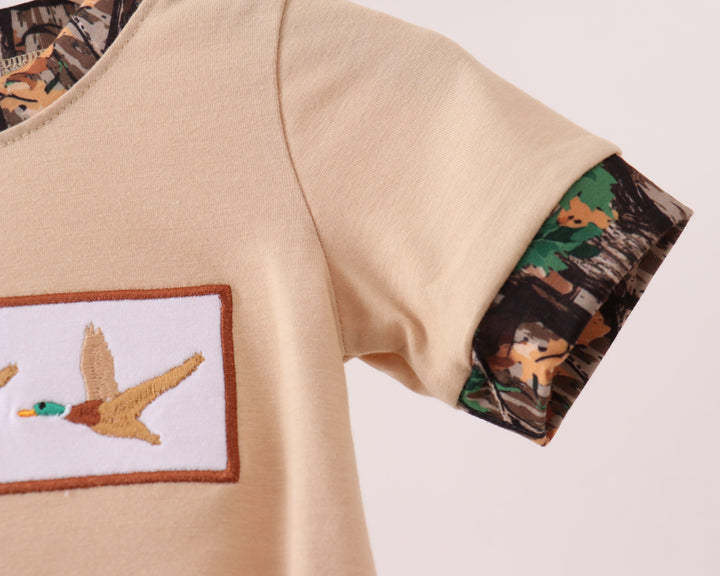 Beige shirt with duck hunting-themed patch and sleeve design on a light gray background